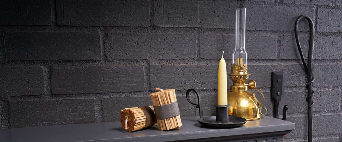 Brass oil lamp, beeswax candle in an iron chamberstick and fire starters on a charcoal mantel